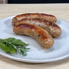 Tre succulente salsicce dorate in padella, servite su un piatto con rosmarino e alloro.