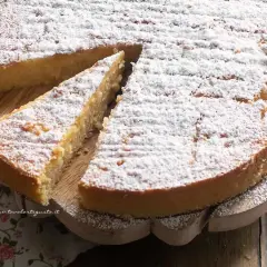Una deliziosa torta di riso, cosparsa di zucchero a velo, su un tagliere di legno. Una fetta è già stata servita.