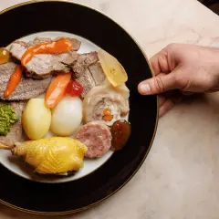 Piatto ricco con bollito di carne, pollo, salumi, verdure e salse, servito su un piatto elegante.