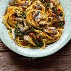 Un piatto invitante di pasta con le sarde, condita con erbe aromatiche, pinoli e pangrattato tostato.