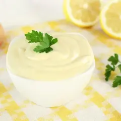 Una ciotola di cremosa maionese fatta in casa, guarnita con prezzemolo. Ingredienti freschi come uovo e limone sullo sfondo.
