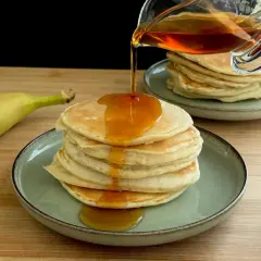 Pancake alla banana con sciroppo d'acero che cola su una pila di soffici pancake.