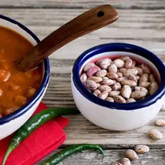 Un piatto fumante di fagioli alla messicana, con peperoncini verdi e una ciotola di fagioli crudi, pronti per un sapore piccante.
