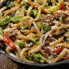 Spaghetti di soia con verdure miste, carne e semi di sesamo in una padella scura.