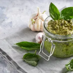 Vaso di vetro pieno di pesto fatto in casa, con aglio e basilico fresco. Perfetto per la pasta al pesto.