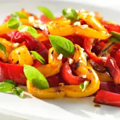 Peperoni arrostiti, rossi e gialli, conditi con aglio e basilico fresco. Un'idea gustosa per le tue ricette con peperoni.