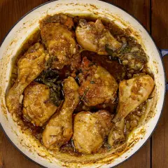 Succulento pollo alla birra cotto in una casseruola, con pezzi dorati e succosi immersi in un sugo aromatico con erbe.