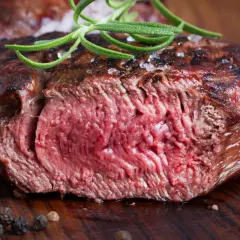 Succulenta tagliata di manzo al sangue, guarnita con rosmarino fresco e sale grosso, su un tagliere di legno.