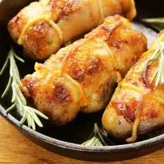Involtini di pollo in padella, dorati e succulenti, con rametti di rosmarino fresco.