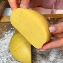 Mani che tengono un impasto giallo, profumato alla vaniglia, pronto per diventare una deliziosa pasta frolla senza burro.