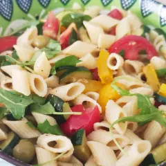 Un piatto colorato di pasta con verdure fresche: zucchine, pomodori, peperoni e rucola.