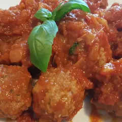 Polpette di carne morbide in un sugo rosso ricco, guarnite con foglie di basilico fresco.