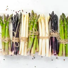 Asparagi verdi, bianchi e viola legati con spago, pronti per scoprire come cucinare gli asparagi. Spezie sparse.