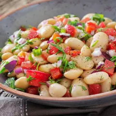 Insalata di fagioli bianchi, pomodori, cipolla rossa e erbe fresche, condita con spezie. Un piatto colorato e gustoso.