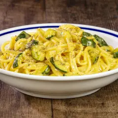 Spaghetti with zucchini and creamy sauce in a white bowl with blue trim on a wooden table.