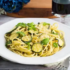 Un piatto di spaghetti con zucchine e menta fresca, un classico della pasta e zucchine alla siciliana, guarnito con parmigiano grattugiato.