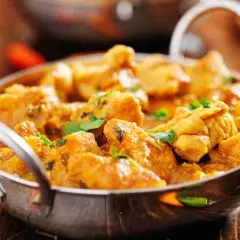 Un invitante pollo al curry cremoso, guarnito con coriandolo fresco, servito in una ciotola metallica su un tavolo di legno.