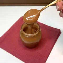 Un cucchiaio d'oro raccoglie un cremoso dulce de leche da un vasetto su un tovagliolo rosso.