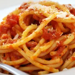 Un piatto di bucatini fumanti conditi con un ricco sugo all'amatriciana ricetta della nonna, spolverato di pecorino.