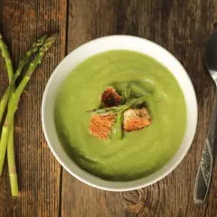 Crema di asparagi vellutata, guarnita con crostini e asparagi freschi, su un tavolo di legno rustico.