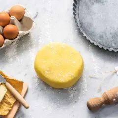 Impasto giallo brillante per pasta frolla senza glutine, pronto per essere steso. Ingredienti freschi e teglia per crostate a portata di mano.