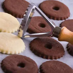Biscotti al cacao e chiari, alcuni con foro centrale, pronti per essere infornati. Un tagliabiscotti con manico in legno è appoggiato su di essi.