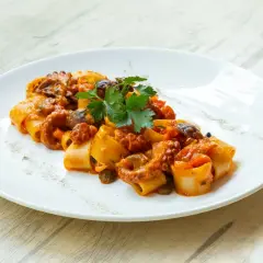 Piatto di paccheri con ragù di polpo, pomodorini e capperi, guarnito con prezzemolo fresco.