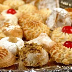 Vassoio pieno di biscotti alle mandorle, alcuni decorati con ciliegie rosse, mandorle e pistacchi.