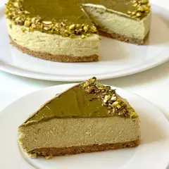 Una fetta di goloso cheesecake al pistacchio, con la torta intera sullo sfondo.