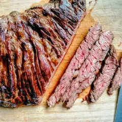 Diaframma di manzo grigliato, tagliato a fette sottili su un tagliere di legno. La carne è succulenta e ben cotta, con striature di grasso che la rendono ancora più invitante.