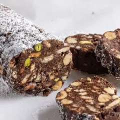 Salame di cioccolato senza uova ricetta della nonna, con biscotti, nocciole e pistacchi, spolverato di zucchero a velo.