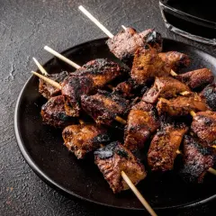 Spiedini di carne succulenti e grigliati, pronti per essere gustati con una salsa scura in un piattino.