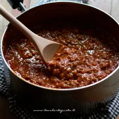 Un pentolone pieno di ragù alla bolognese, pronto per condire la pasta. Un cucchiaio di legno mescola la salsa ricca e saporita.