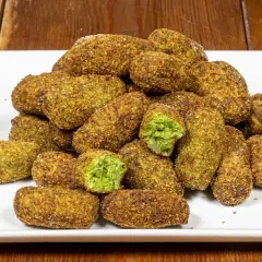 Un mucchio di polpette di broccoli dorate e croccanti su un piatto bianco. Alcune sono tagliate a metà, rivelando il ripieno verde brillante.