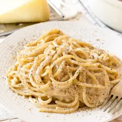 Un piatto di spaghetti fumanti, conditi con la cremosità del cacio e pepe, cosparsi di pepe nero macinato fresco.