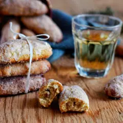 Ciambelline al vino dorate e zuccherate, una invitante pila legata da un nastro bianco, accanto a un bicchierino di vino e cannella.