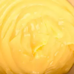 Close-up of smooth, creamy yellow pastry cream in a bowl, with visible swirls and highlights.