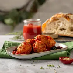 Polpette di cavolfiore dorate e saporite, immerse in un sugo rosso, servite con pane rustico e un rametto di erbe aromatiche.