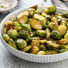 Ciotola piena di cavoletti di Bruxelles arrostiti, dorati e saporiti, guarniti con erbe fresche.