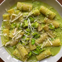 Rigatoni conditi con una cremosa salsa verde e fave fresche, guarniti con scaglie di parmigiano e pepe nero. Un piatto di pasta e fave che profuma di primavera.