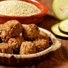 Polpette di melanzane al forno dorate e croccanti, servite in una ciotola rustica, con melanzane fresche e quinoa sullo sfondo.
