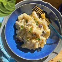 Creamy pasta with cauliflower, pine nuts, and herbs on a blue plate with a gold fork.