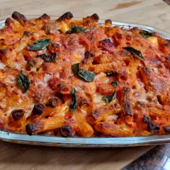 Un invitante piatto di pasta al forno napoletana, con pasta rigata dorata, sugo rosso e formaggio fuso, guarnito con foglie di basilico fresco.