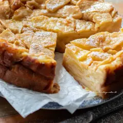 Una deliziosa torta di mele dorata, con fette di mela caramellate in superficie e una spolverata di zucchero a velo.