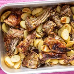 Succulento abbacchio al forno con patate dorate, profumato al rosmarino, servito in una teglia d'argento su un tavolo rosa acceso.