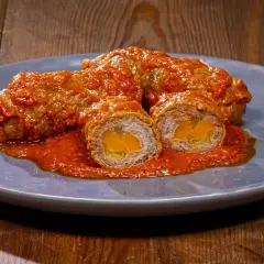 Involtini alla romana succulenti, avvolti in un sugo rosso intenso, con un cuore dorato visibile in sezione.