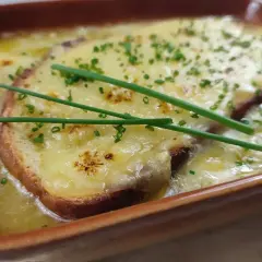 Zuppa di cipolle fumante, con crostini dorati e formaggio filante, guarnita con erba cipollina fresca.