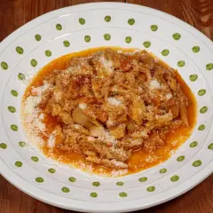 Un piatto di trippa alla fiorentina, saporita e ricca, cosparsa di parmigiano grattugiato, servita su un piatto bianco decorato.