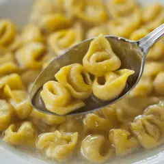 Un cucchiaio raccoglie deliziosi tortellini fatti in casa in brodo, pronti per essere gustati.
