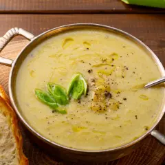Una ciotola di cremosa crema di patate, guarnita con cipollotto fresco e pepe nero, servita con fette di pane tostato.